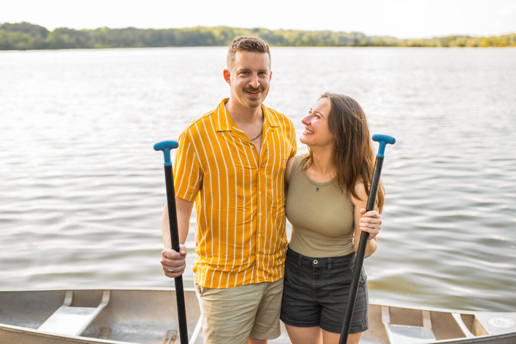 Engaged couple stands by canoe smiling happily in Eagle Creek Park in Indianapolis.