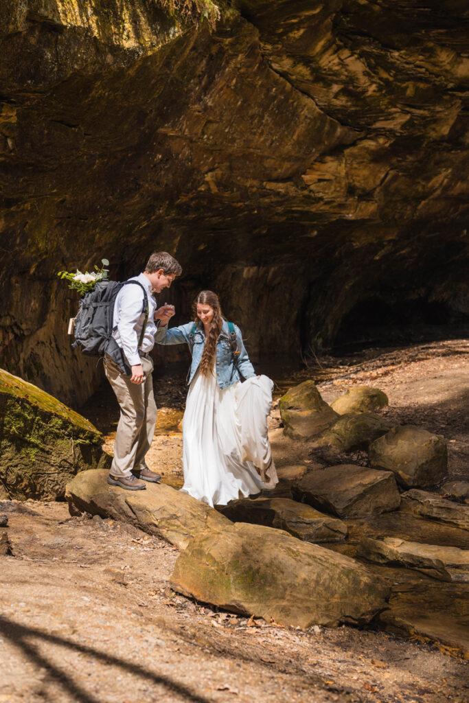 Groom helps bride as they hike on their wedding day.