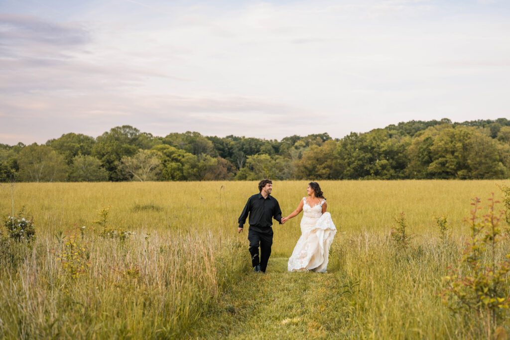 Bride and groom running through a field holding hands.