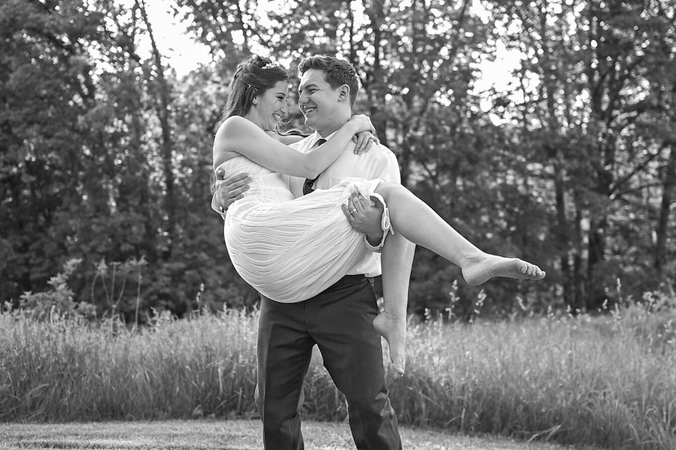 Groom picks up bride in a grassy meadow.