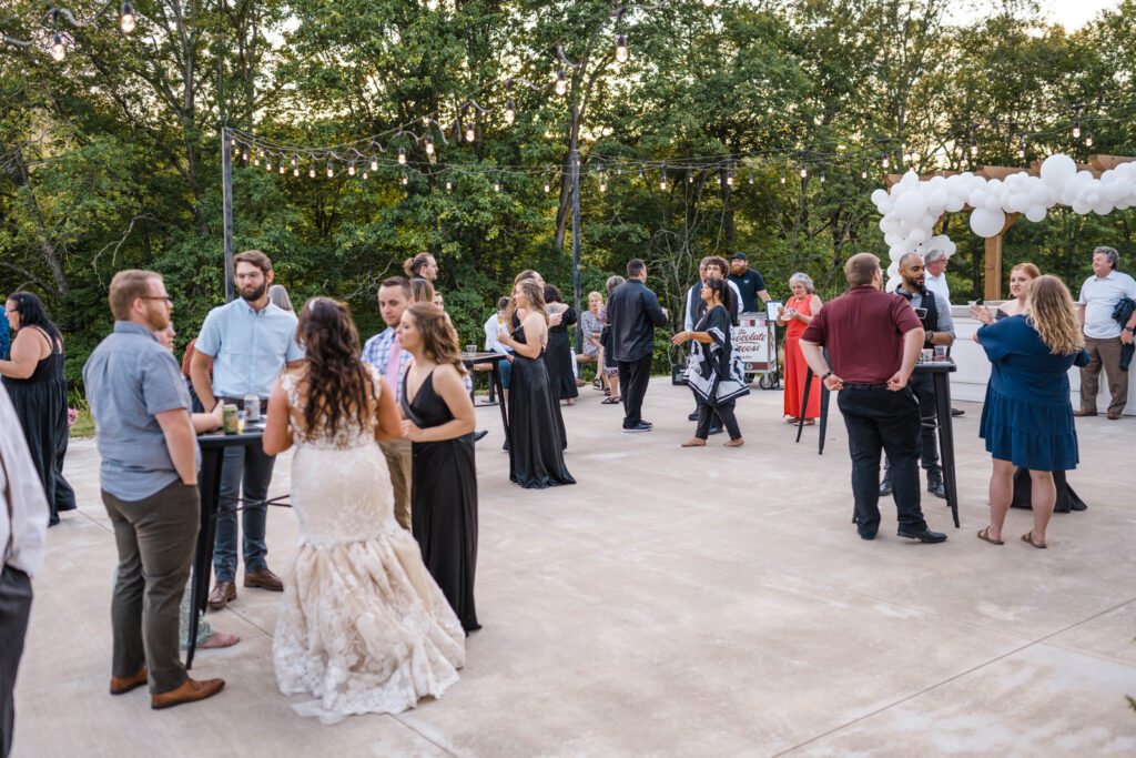 Guests mingle in an open-air patio under string lights during wedding reception.