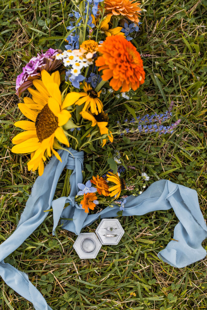 Bouquet of wildflowers rests in the grass with bride and groom's rings at their wildflower elopement.