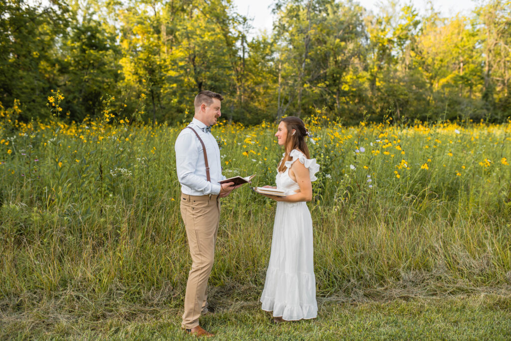 Bride and groom share private vows at their wildflower elopement in front of a pollinator habitat field.