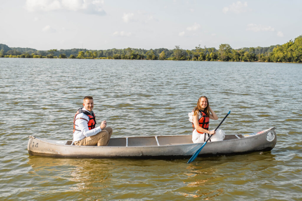 Bride and groom smile in canoe dressed in their wedding attire.