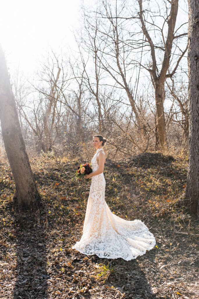 Bride standing in the woods holding flowers.