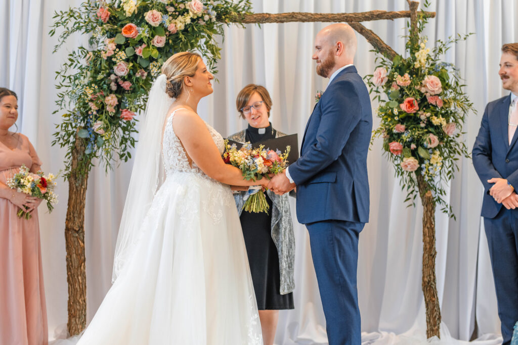 Bride and groom holding hands during indoor wedding ceremony at One World at Woolery Mill.
