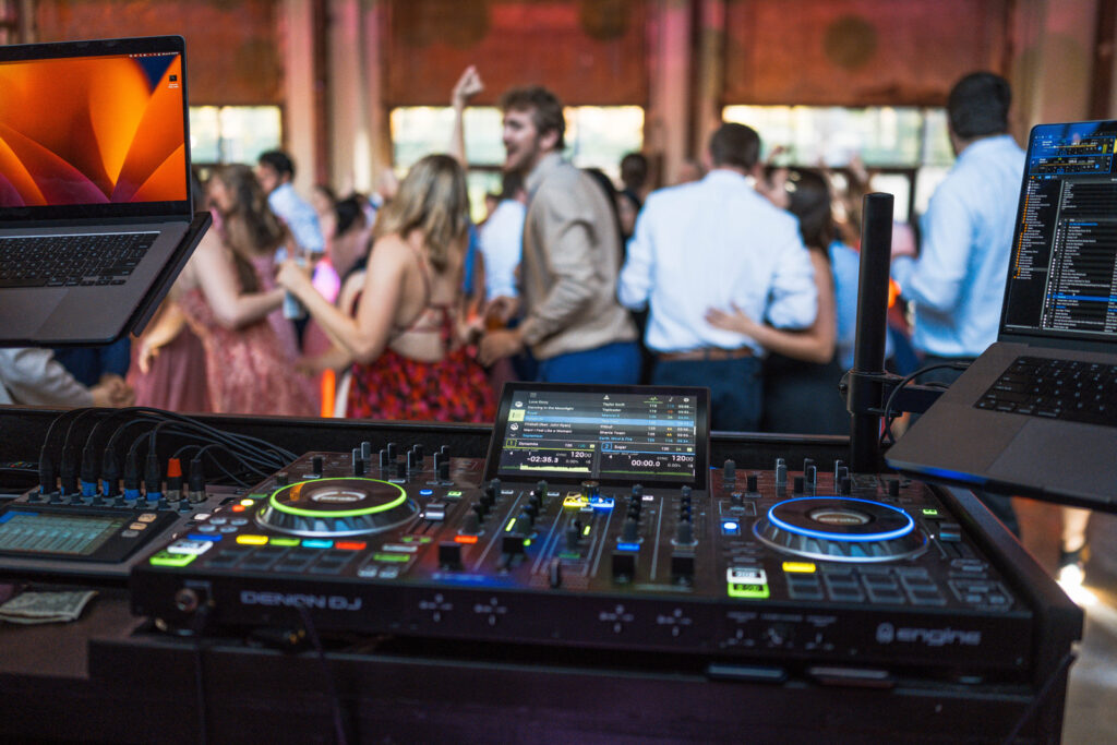 DJ's mixing deck at wedding reception with people dancing.
