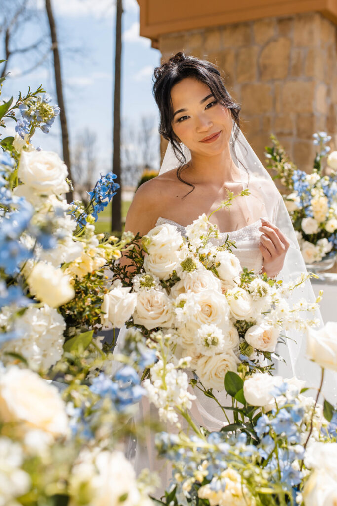 Bride at Lizton Lodge Wedding Venue smiles while standing amidst blue and white flowers.