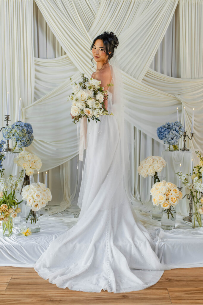 Brides portraits in front of white draping with blue and white flowers.