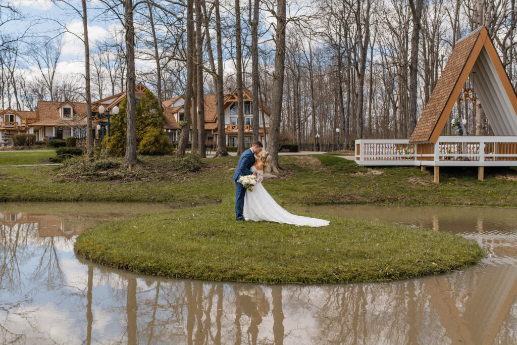 Bride and groom kiss by pond at Lizton Lodge Wedding Venue.