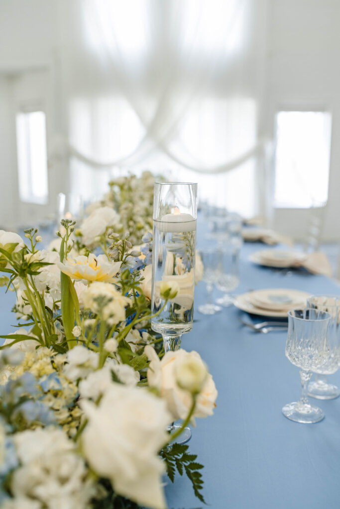 Centerpiece of table at wedding reception with blue table cloth, white flowers, and floating candles.