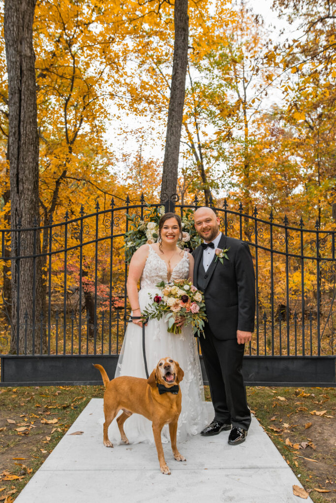 Bride and groom smiling with their dog on their wedding day.