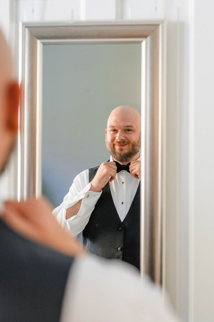 Groom fixes bowtie in mirror.