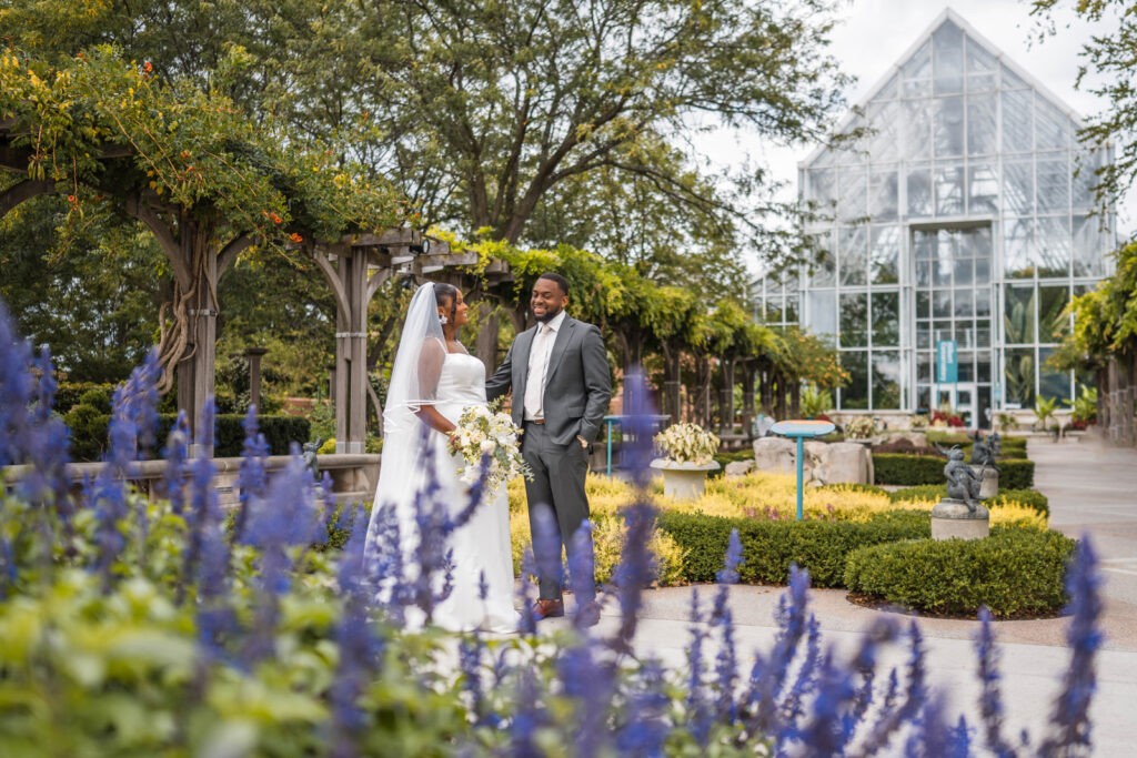Couple smiling happily at White River Gardens with purple flowers in foreground.