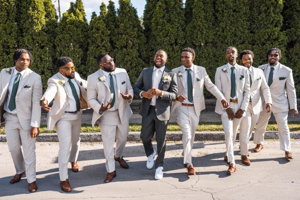 Groom laughing with groomsmen while walking in front of cypress trees.
