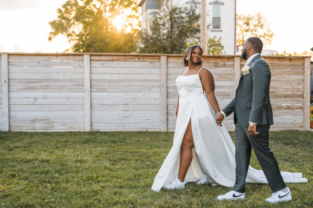 Bride and groom hold hands at sunset walking in a grassy area at Ivory Foundry Weddings & Events.