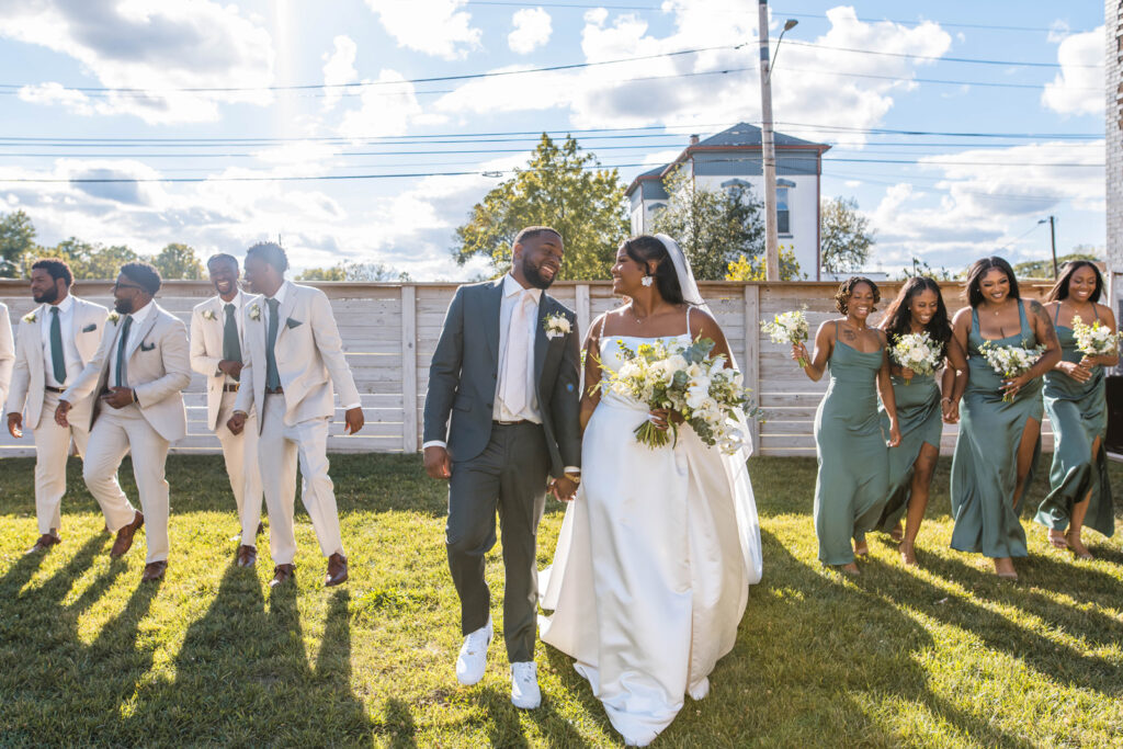 Bride and groom holding hands while walking alongside their wedding party.