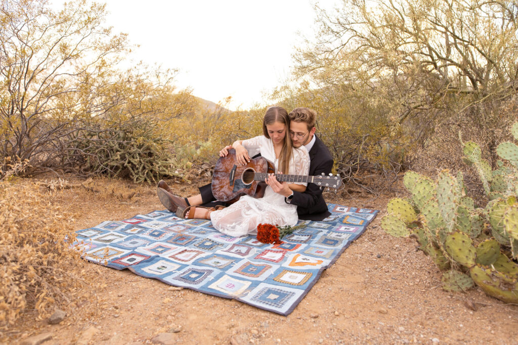 Bride and groom sitting on a blanket during their outdoor elopement to play guitar.