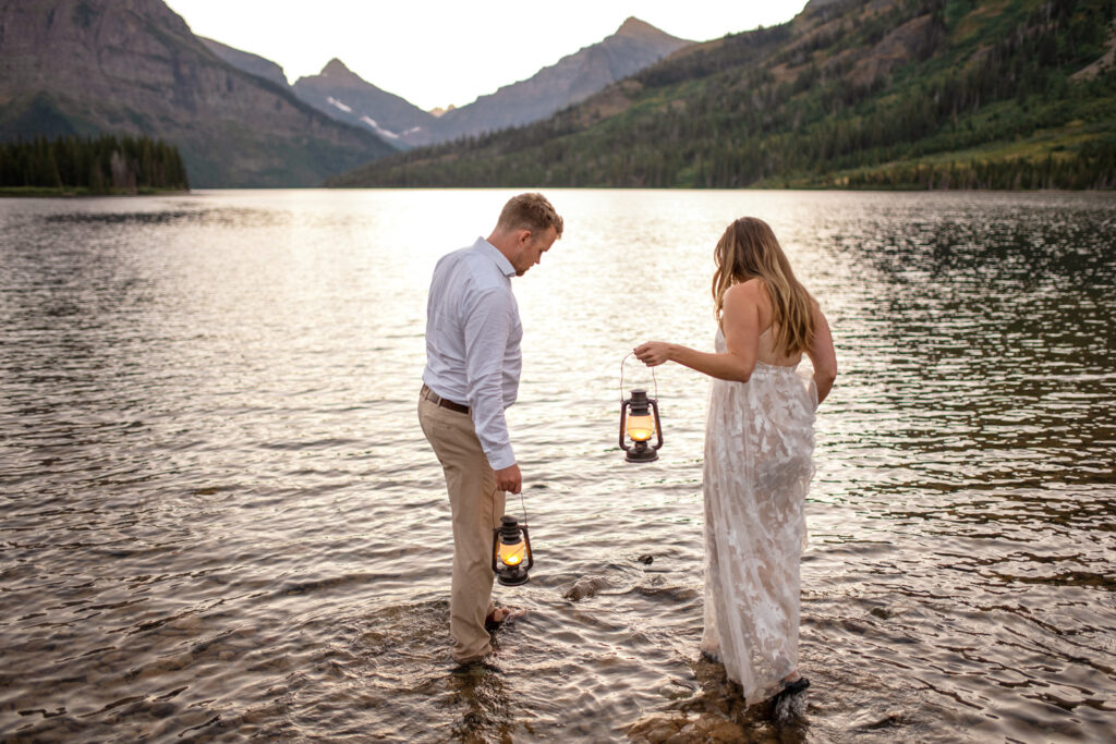 Couple wades into water carrying lanterns.