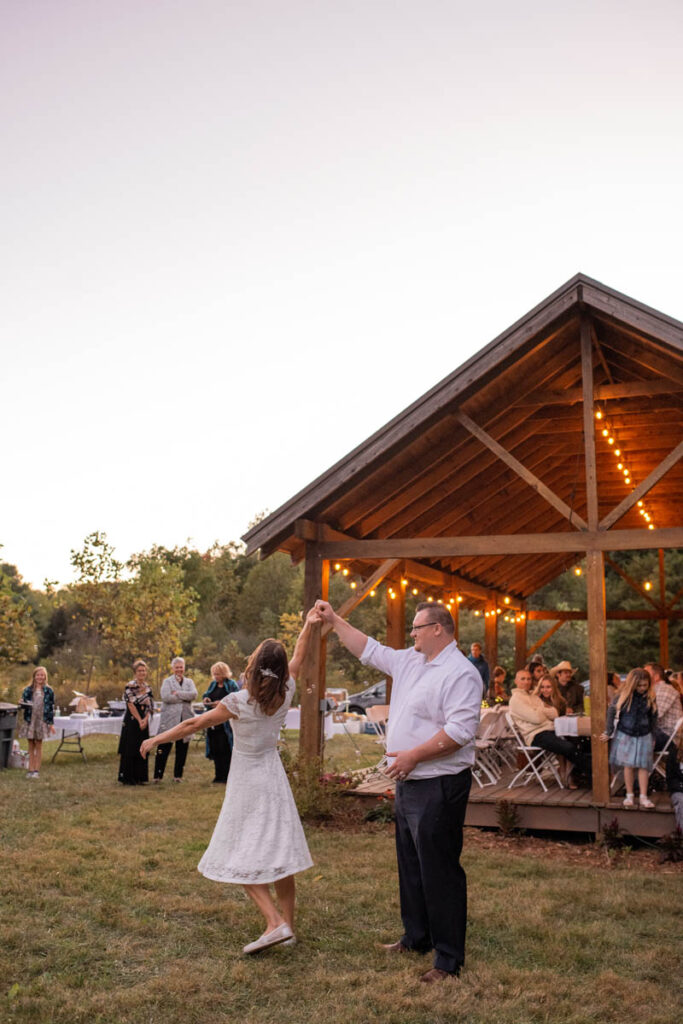 Bride and groom have a first dance in front of a lit pavilion and guests.