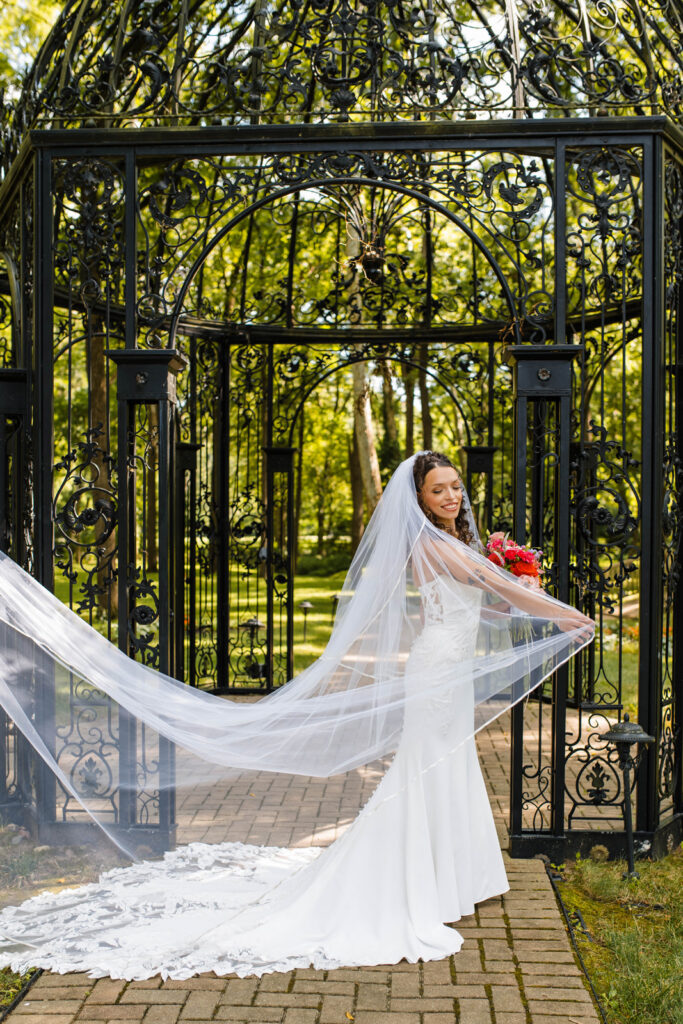 Bride plays with her veil in front of gazebo.