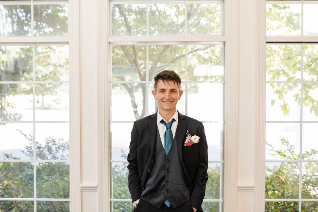 Groom smiling in front of windows.