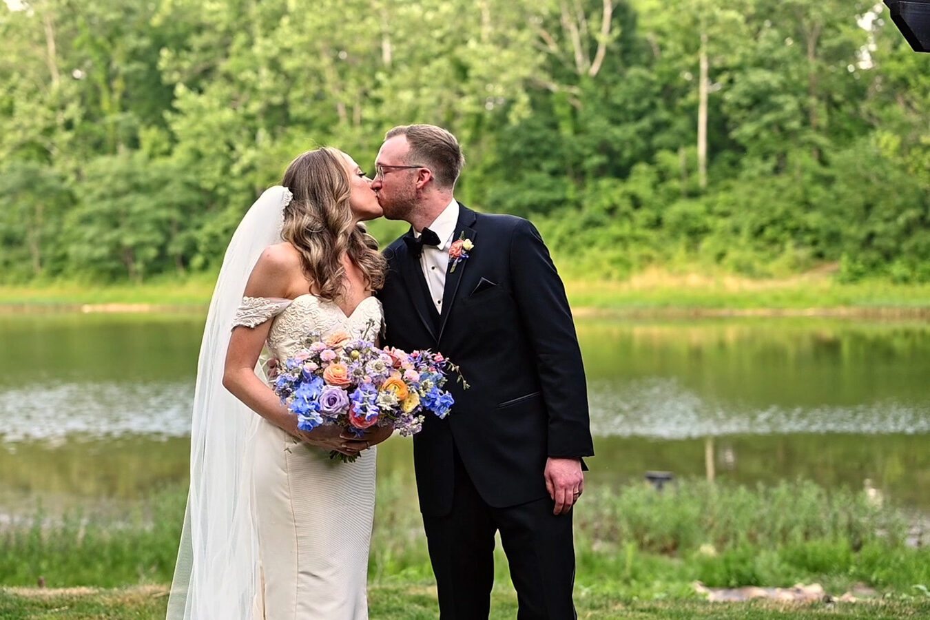 Couple shares a kiss in front of lake in the summertime at The Conservatory at Evergreen.