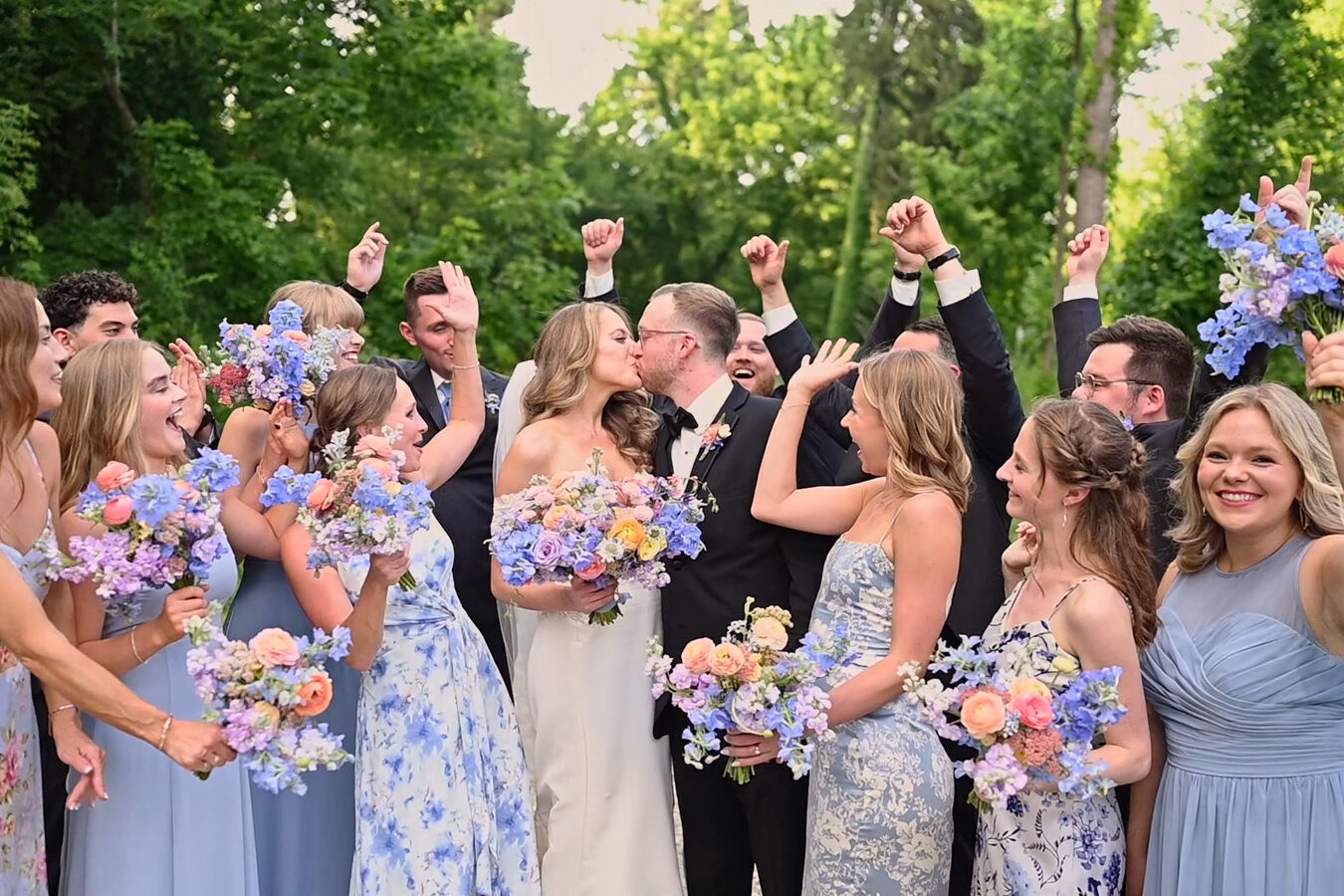 Bride and groom kiss while wedding party cheers for them at wedding at The Conservatory at Evergreen