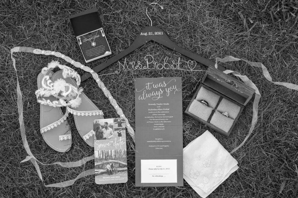 Flat lay image of wedding items including rings, shoes, jewelry, and invitations in the grass at an Indiana outdoor wedding.