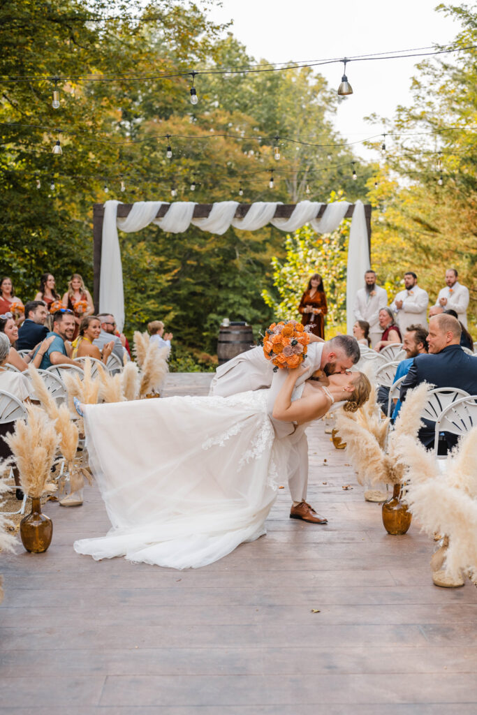 Bride and groom share a dip kiss at the end of their outdoor ceremony at The Barn at Timber Ridge.