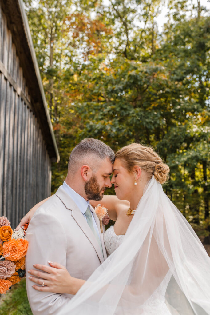 Bride and groom rest their heads together while the bride's veil flows around them next to The Barn at Timber Ridge.