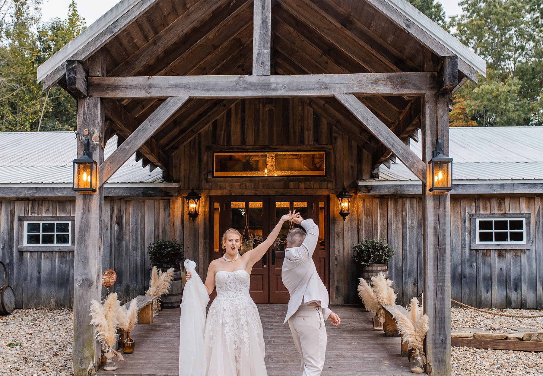Couple laugh as they twirl one another in front of a barn.